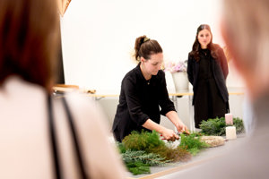 Eine Frau zeigt den Teilnehmer:innen des Advent-Hocks im Festspielhaus Bregenz das Adventkranzbinden