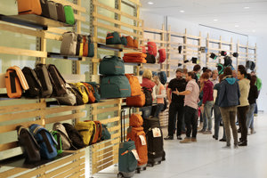 Messe-Besucher:innen vor hohen Holzregalen mit Taschen und Rucksäcken im Foyer des Festspielhauses Bregenz