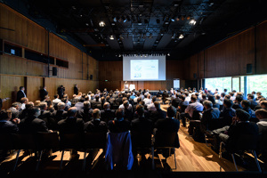 Vollbesetzte Reihenbestuhlung, eine Bühne mit Rednerpult und großer Leinwand im Seestudio im Festspielhaus Bregenz
