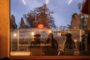 © Hanno Mackovitz LandStadt Vorarlberg. Drei junge Menschen sitzen auf einer verglasen Terrasse © Hanno Mackovitz