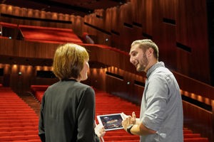 Zwei Personen unterhalten sich vor dem rot bestuhlten aufsteigenden Auditorium im Großen Saal des Festspielhauses