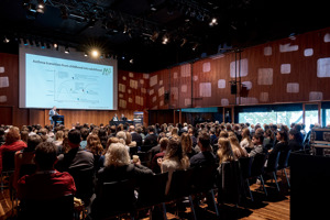 Menschen sitzen in Stuhlreihen vor einer Bühne mit einer großen Leinwand im Seestudio