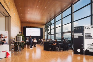 Tagungsteilnehmer:innen in Reihenstuhlung im Seefoyer im Festspielhaus Bregenz mit Blick auf den See