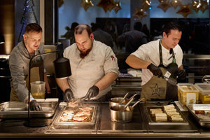 Drei Köche arbeiten konzentriert in der Showküche vor der Fensterfront des Seefoyers im Festspielhaus
