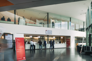 Kongressteilnehmer:innen stehen vor dem Registrierungstresen im Eingangsfoyer des Festspielhauses