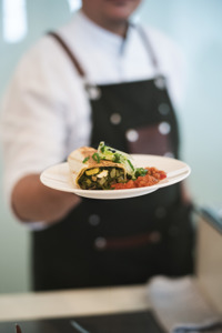 Ein Koch hält einen garnierten Teller Richtung Kamera im Festspielhaus Bregenz
