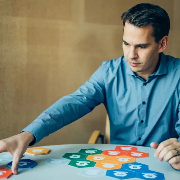 Ein Mann in blauem Hemd sortiert wabenförmige Karten auf einem Tisch © Lukas Zenk