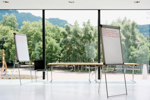 zwei beschriebene Flipcharts stehen vor eine großen Fensterfront mit Blick auf viele Bäume