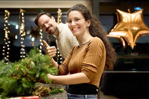 Eine Frau hält einen Adventkranz hoch und zeigt mit dem Daumen nach oben