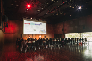 Kongressteilnehmer:innen sitzen in schwarzen Stuhlreihen vor einer großen Leinwand im abgedunkelten Seestudio