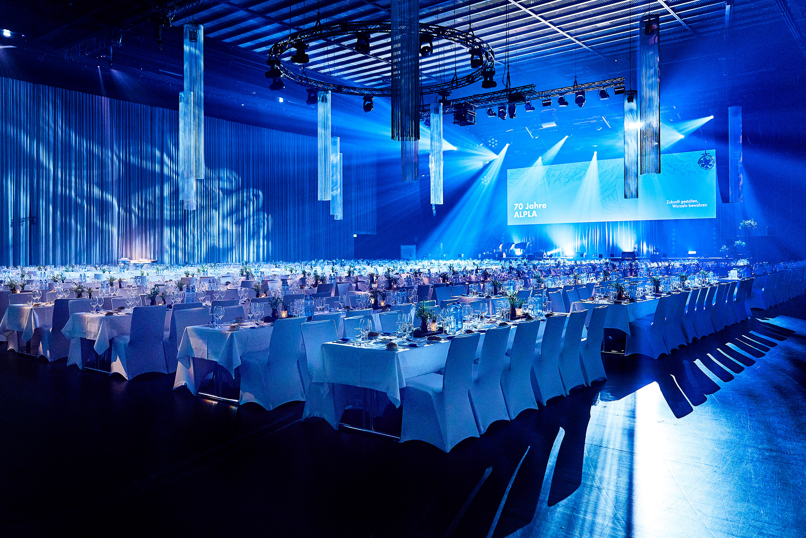 blau eingeleuchtete Werkstattbühne mit weiß gedeckten Tischreihen und Stuhlhussen © Anja Koehler