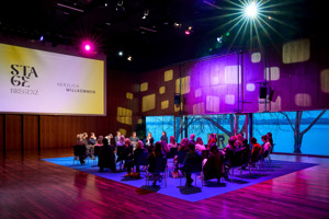 Kongress-Teilnehmer:innen sitzten auf schwarzen Stühlen verteilt auf einem blauen Teppich im Seestudio